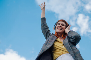 Happy businesswoman listening to music with headphones and dancing under blue sky