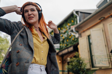 Stylish redhead woman listening music with headphones in urban city