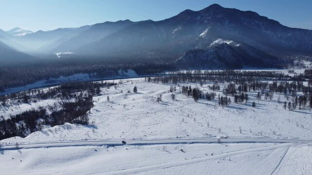 Drone footage of snowy mountains, valleys, and forests in Ust-Koksa, Altai Republic, Russia, under clear skies, showing the remote region&rsquo;s beauty during winter.