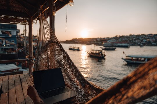 A digital nomad working on a laptop while sitting on a hammock outdoors. The person is enjoying a remote work setup in a relaxing environment.