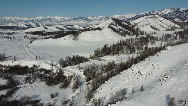 Drone footage of snowy mountains, valleys, and forests in Ust-Koksa, Altai Republic, Russia, under clear skies, showing the remote region&rsquo;s beauty during winter.