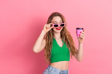 Stylish young woman in a green top enjoying coffee with a cheerful smile against a vibrant pink background