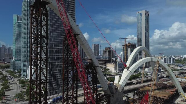 Low angle view of massive steel bridge pylons under construction of Miami Signature Bridge, with temporary support towers against a blue sky	