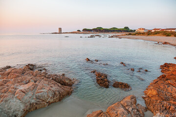 Rocky Mediterranean shoreline with clear water and ancient tower at peaceful coastal village during sunset