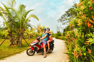 Funny authentic young happy caucasian couple pose on scooter together with palm trees, having fun driving red scooter on tropical road trip in southeast asia. Couple in love having fun travel in asia