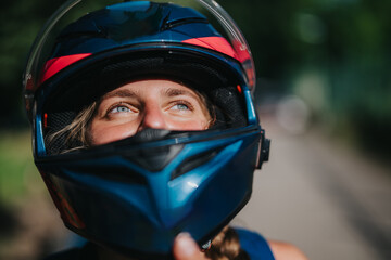 Portrait of a person wearing a motorcycle helmet, gazing upwards in a sunny outdoor setting. The...