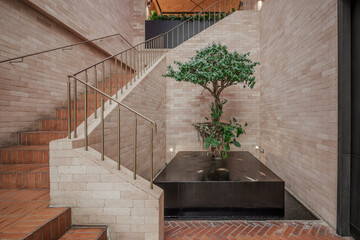 Modern interior with a brick wall and staircase. A small Ficus tree grows from a water feature,...