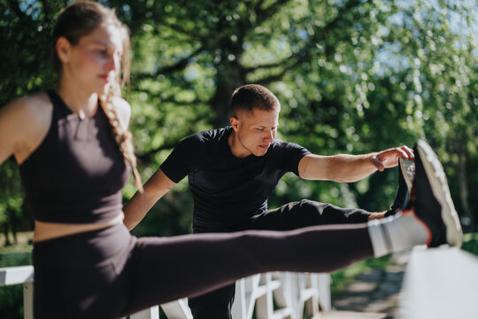 A man and a woman stretching together on a railing in a serene green park on a sunny day, enhancing their fitness and flexibility while enjoying the natural surroundings and fresh air. - Powered by Adobe