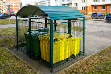 Recycling station with yellow and green bins secured under a metal shelter in a residential area