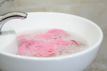 Close up of soaking pink cloth in a white sink. The setting a bathroom with simple decor. Concept of daily stains on clothes