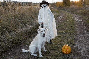 child in a white blanket, hat and black glasses walks his beloved white dog. person in ghost...