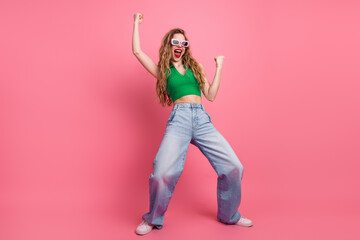 Excited young woman in stylish casual outfit posing against pink background, expressing joy with a...