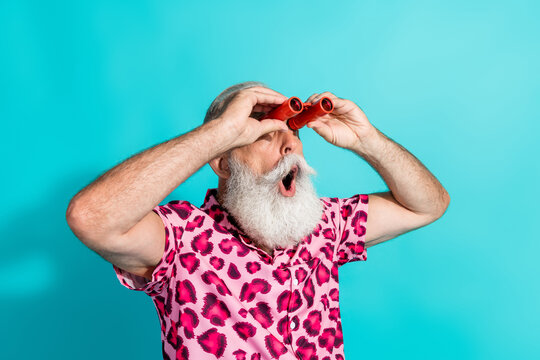Photo of cool retired bearded male amazed look binoculars empty space wear pink leopard print outfit isolated on aquamarine background - Powered by Adobe