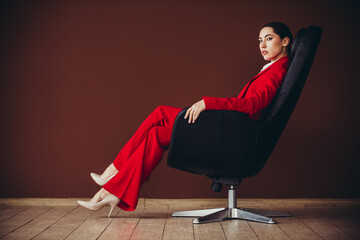 Confident Young Businesswoman in Elegant Red Suit Sitting in Modern Office Chair
