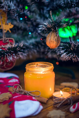 A candle is burning under the Christmas tree, near are cookies, candy, wool socks and mittens