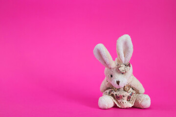 Toy white cartoon rabbit sits on a pink background