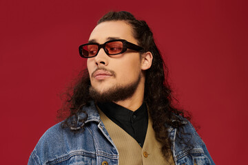 Handsome young man with a beard showcases unique style against a bold red backdrop
