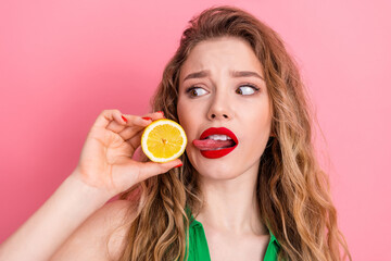 Young woman showing a lemon slice and making a funny face with a pink background, capturing a...