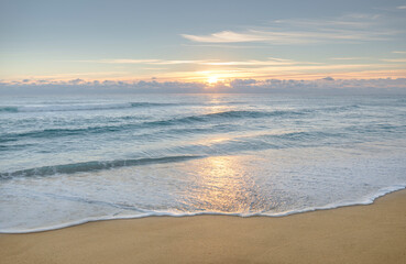 Calm ocean waves on sandy beach at sunrise