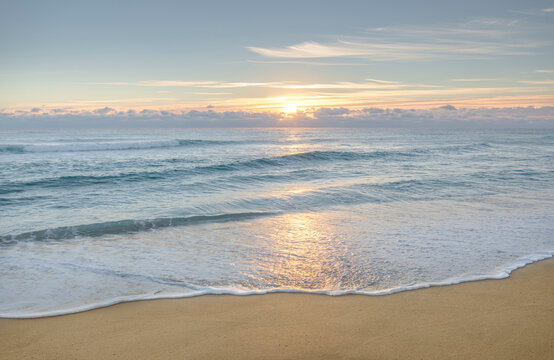 Calm ocean waves on sandy beach at sunrise
