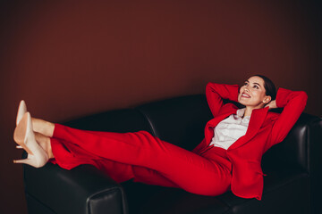 Attractive Confident Businesswoman in Red Suit Reclining on a Black Sofa Displaying Elegance