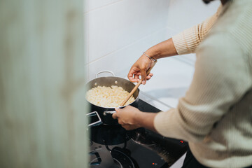 A person stirs pasta cooking in a pot on an electric stove, showcasing a cozy and modern home cooking environment.