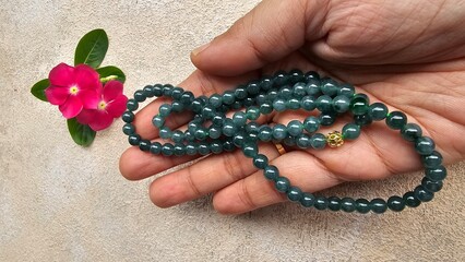A long necklace of natural green at someone hand, green jade with a flower beside it, isolated on a...