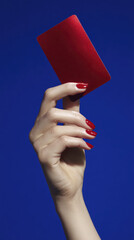 Elegant Hand Presenting a Shiny Red Card Against a Vivid Blue Background with Glamorous Nail Polish