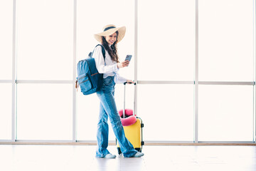 Fashionable young woman at airport terminal ready for travel with suitcase and accessories while...