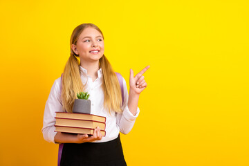 Happy schoolgirl holding books and potted plant while gesturing on bright yellow background