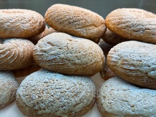 Close-up of oval-shaped cookies sprinkled with powdered sugar, stacked in a bakery display