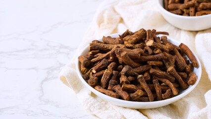 closeup pile of dry dandelion root herb for loose tea in bowl on white table background with copy space