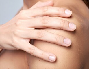 Naklejka premium Close-up of a woman's hand gently touching her shoulder, emphasizing healthy, smooth skin and self-care. Ideal for beauty, wellness, and dermatology concepts.