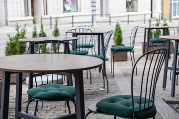 Inviting empty round tables and chairs with green cushions set at an outdoor city cafe patio, ready for urban leisure and relaxation