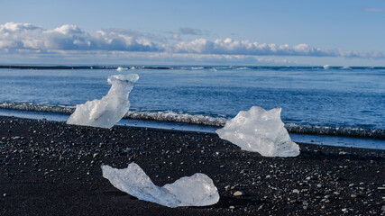 At Diamond Beach in Iceland, glistening icebergs rest on dark volcanic sands. Clear blue skies...