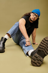 Stylish young man with a beard sitting on the floor in casual attire and a blue beanie