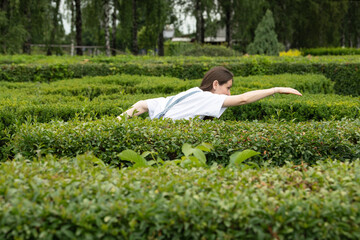 A woman navigates through a dense hedge maze, bending slightly as she explores the twists and...
