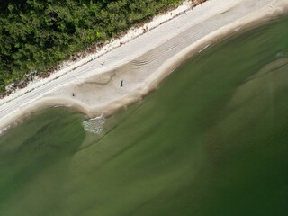 Serene overhead view of secluded sandy beach surrounded by dense forest with gentle waves lapping...