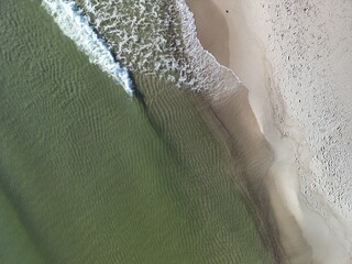 Drone shot of coastal waves meeting sandy beach forming natural white foam curves along the...