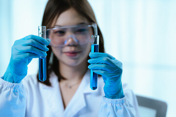 A female scientist conducts research in a modern laboratory, wearing protective gear, analyzing blue liquid in test tubes, focusing on innovation, discovery, accuracy, and medical development.