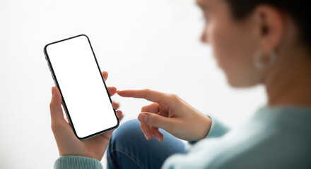 Fototapeta na wymiar Woman holding and pointing at smartphone with blank screen, over shoulder view of person using mobile phone with empty display mockup