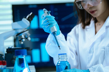 A female scientist in a modern laboratory conducts research using a pipette and microscope, analyzing samples under blue light to develop medical innovations and scientific discoveries.