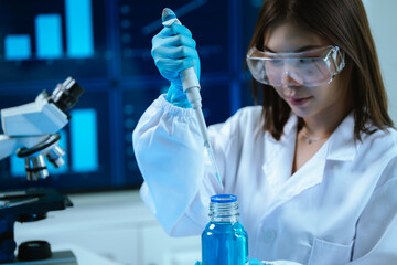 A female scientist in a modern laboratory conducts research using a pipette and microscope,...