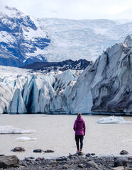 A traveler stands before the awe-inspiring Svinafellsjokull Glacier in Iceland, surrounded by...