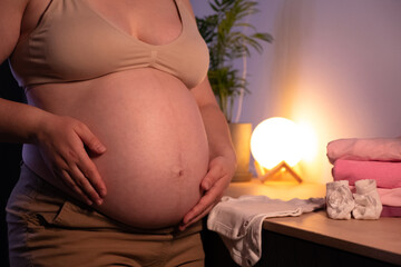 Pregnant woman with big belly in anticipation getting ready for the baby girl at home. Future mom at 9 months of pregnancy preparing and planning newborn baby girl clothes