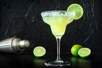 Margarita cocktail in the classic glass, side view on a black background, with limes and a salt...