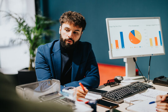 Man in formal attire presenting data charts on a computer screen in an office.