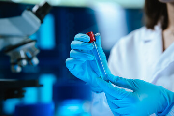 Scientists in lab coats and gloves pour blue liquid from one test tube to another to perform...