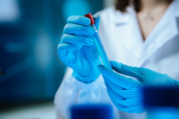 Scientists in lab coats and gloves pour blue liquid from one test tube to another to perform...