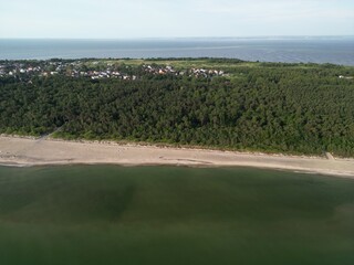Expansive aerial view of forested coastline with sandy beach and calm green waters stretching to...